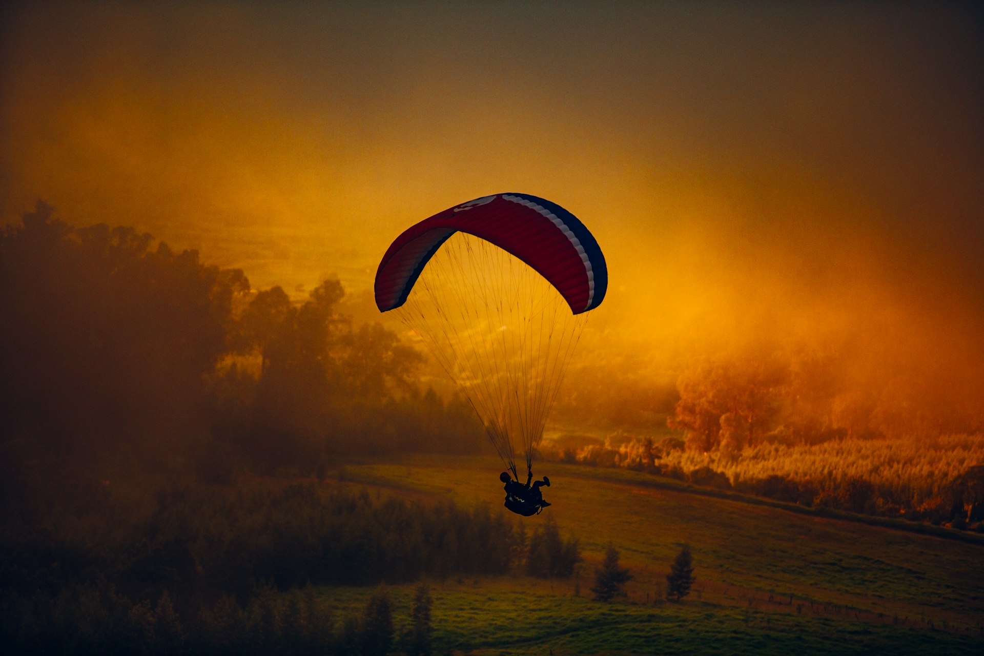 Paraglider gliding through orange sunset clouds