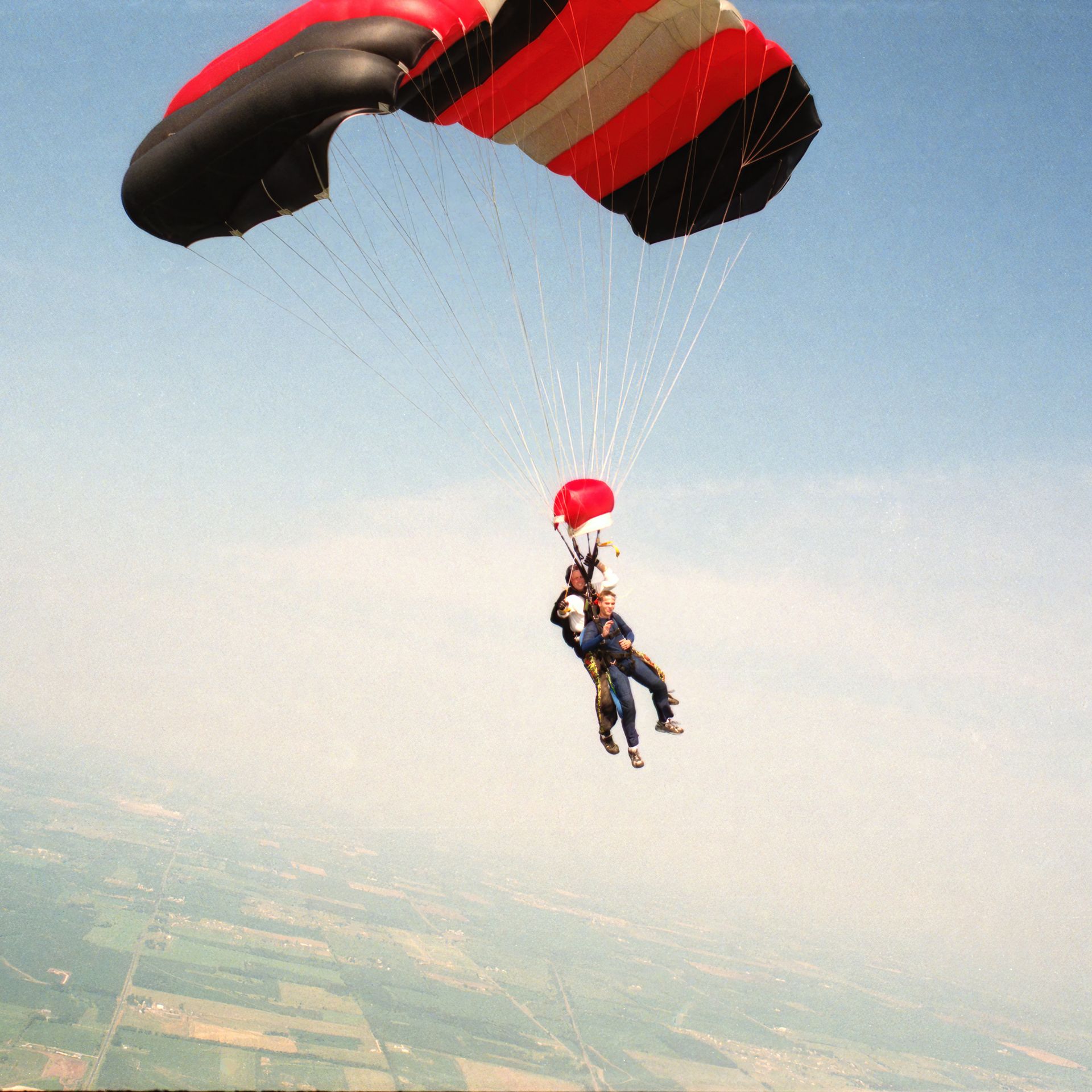 Tandem paraglider drifting over a green valley